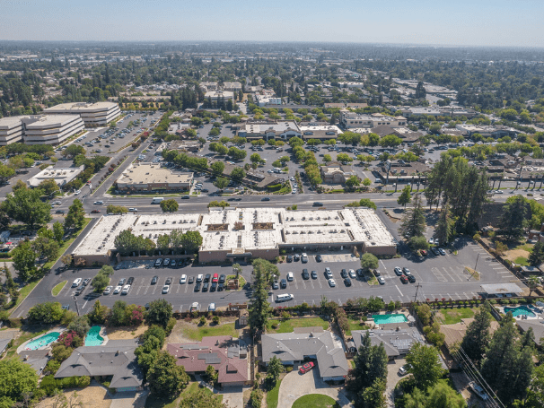 Aerial view of a commercial building with a large parking lot in Fresno, California, surrounded by residential homes, roads, and greenery, highlighting the city's mixed-use urban landscape. Aerial view of a commercial building with a large parking lot in Fresno, California, surrounded by residential homes, roads, and greenery, highlighting the city's mixed-use urban landscape.